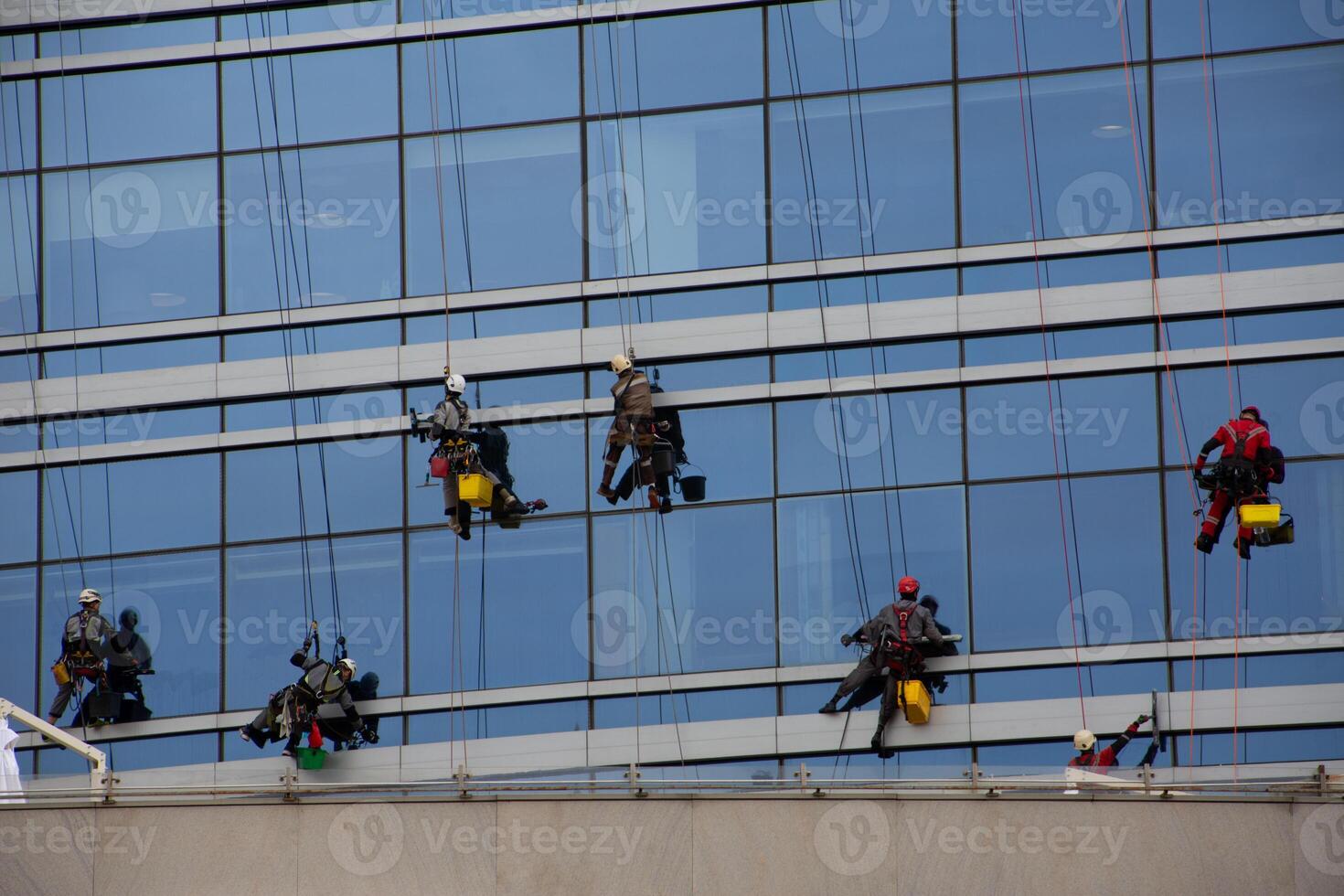Group of climbers clean glass of skyscraper on special mounts with insurance, hard work at height, cleaning the exterior of glass office building photo
