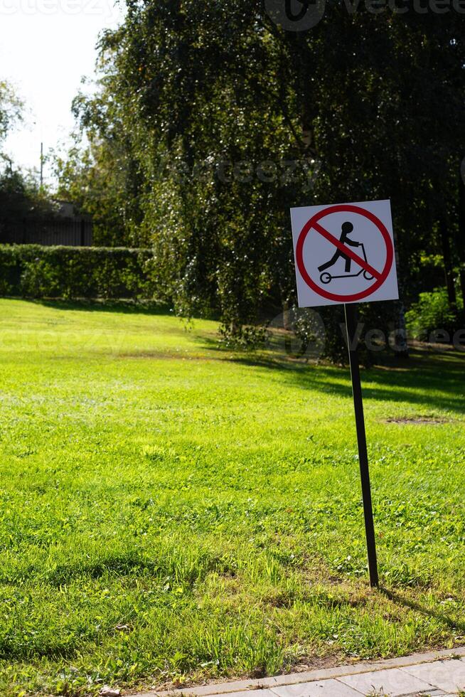 Sign in the park prohibits riding scooter. Road sign regulating traffic on city street. Modern rules for scooters in green field background photo