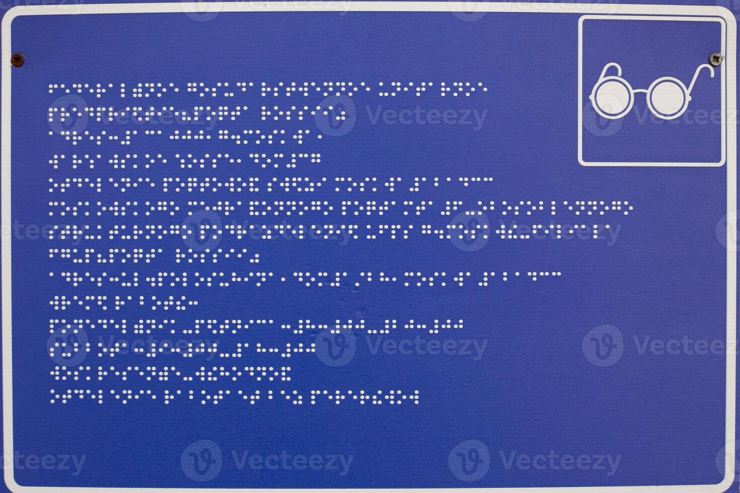 Blue sign with white dots of braille text. Braille alphabet to help people with blindness. Information for people with disabilities in frame with glasses sign photo