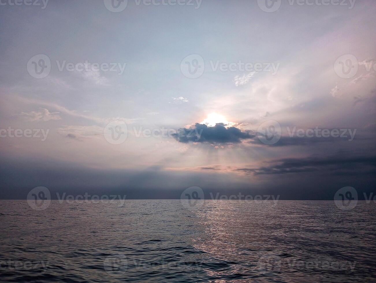A large body of water with a sun shining through the clouds photo