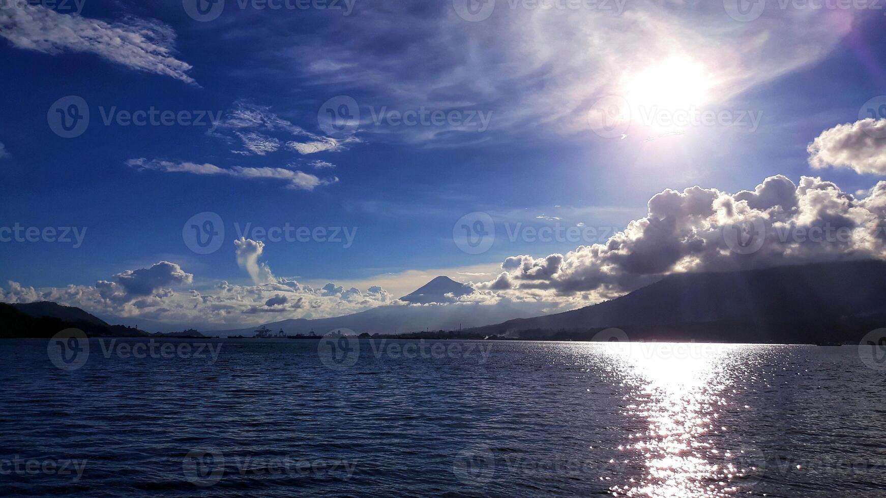 The sun shines brightly over a lake with mountains in the background photo