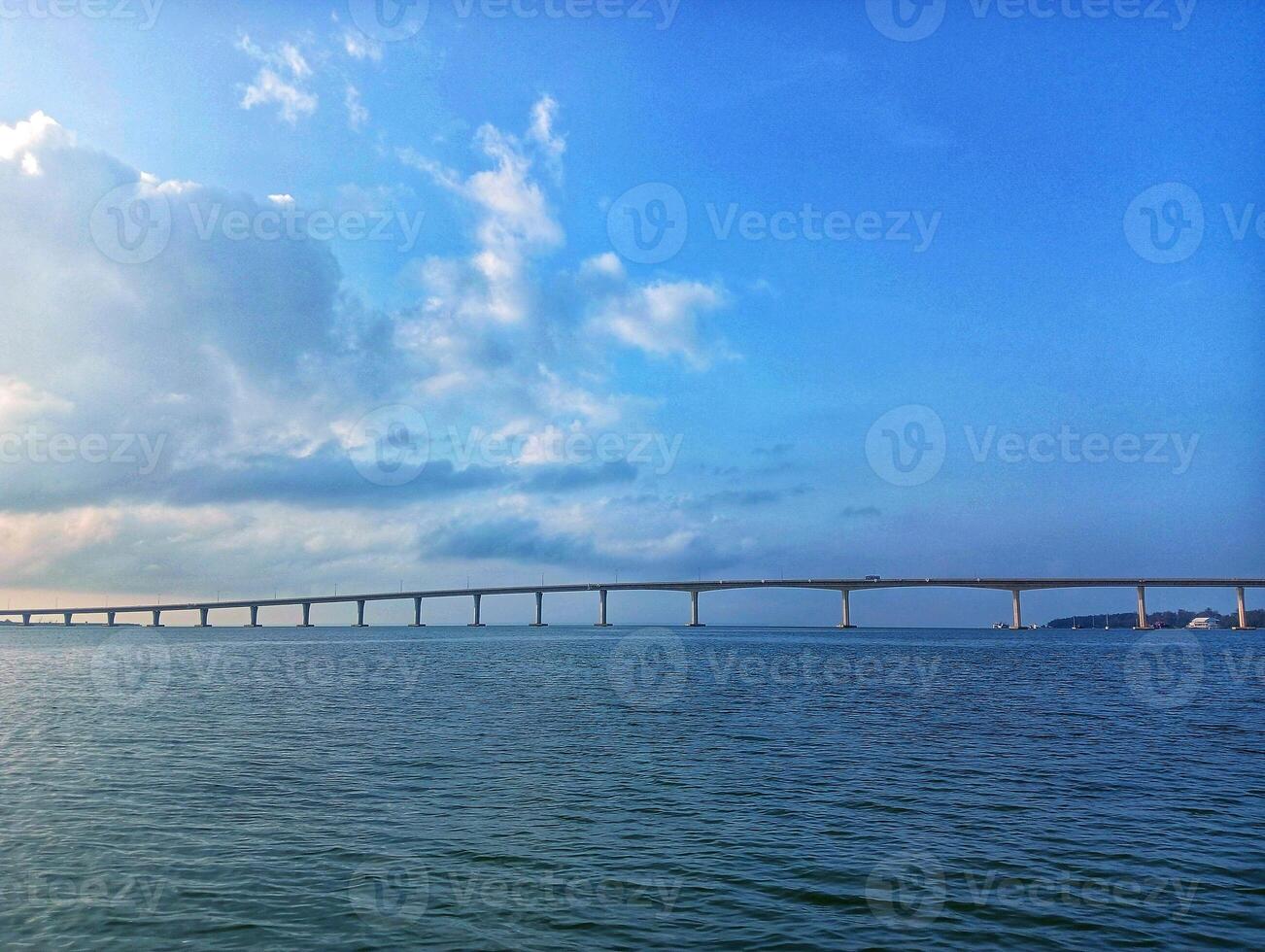 A boat is sailing across the ocean with a bridge in the background photo