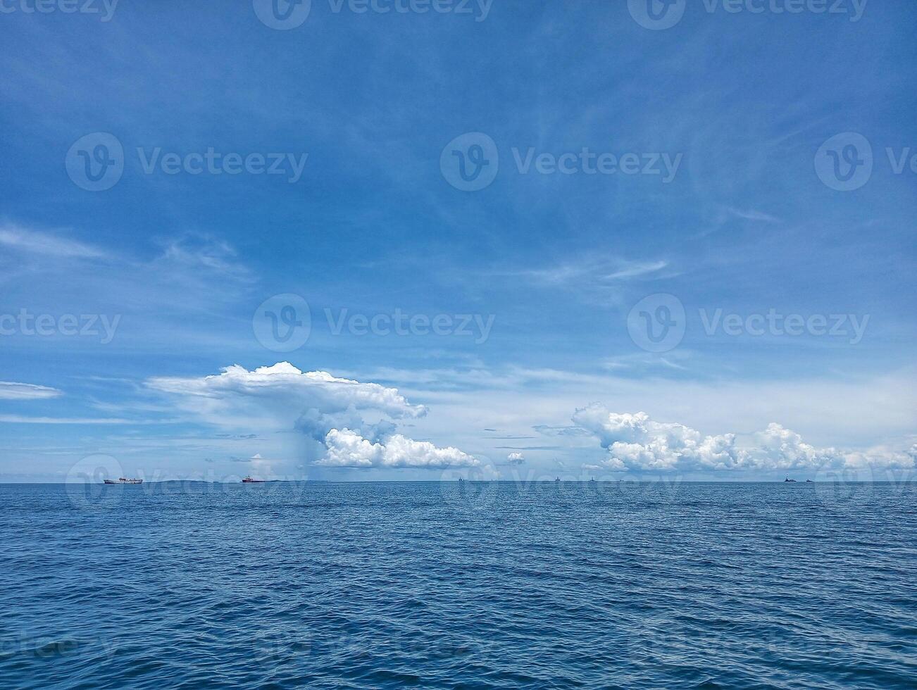 A blue sky with clouds and a boat in the ocean photo