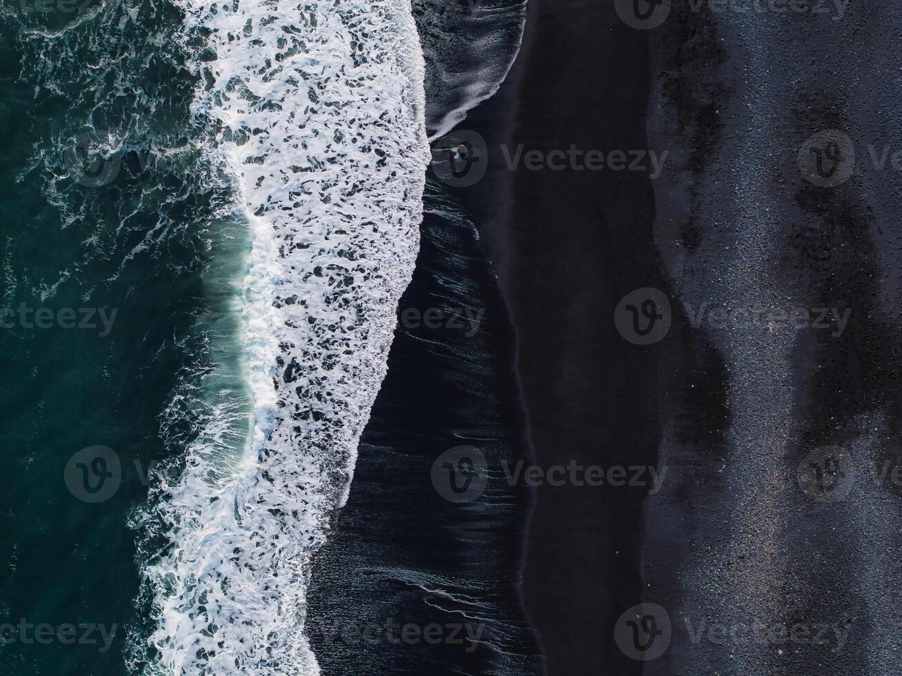 Stunning aerial view of a black sand beach in Iceland, where white foamy waves crash against the shore, creating a striking contrast and visual effect. photo