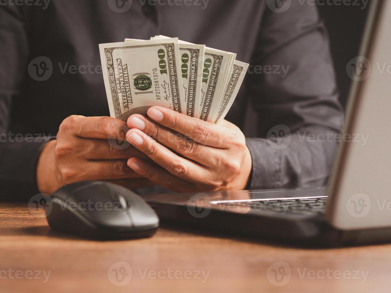 Hand of a businessman in a black shirt holding US dollars banknote while sitting in the office photo