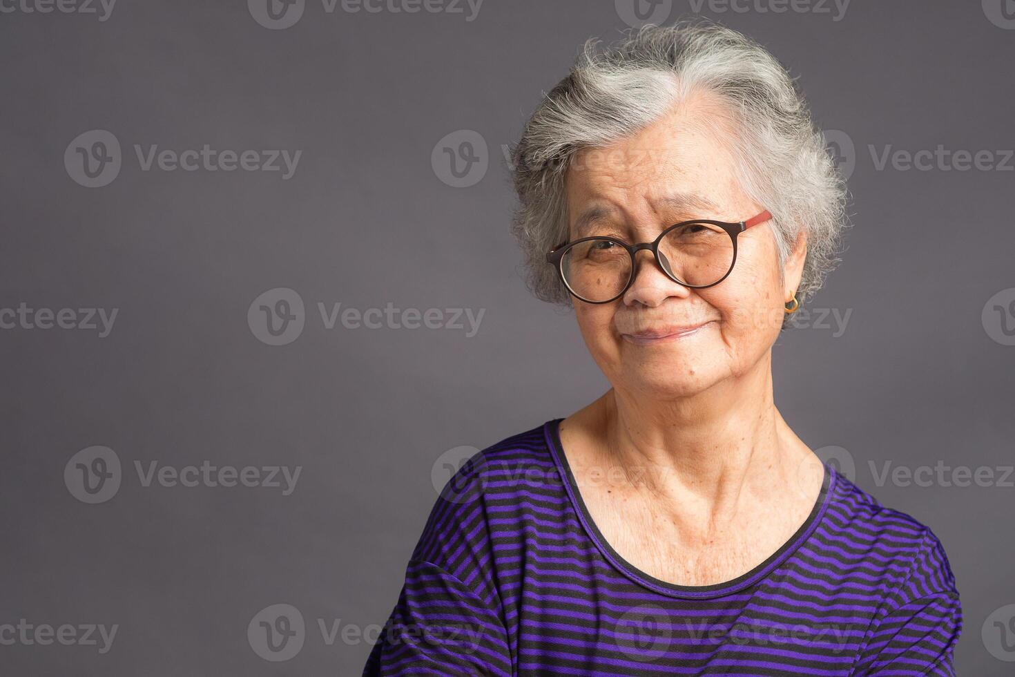 An elderly Asian woman looking at the camera with a smile while standing over a gray background photo
