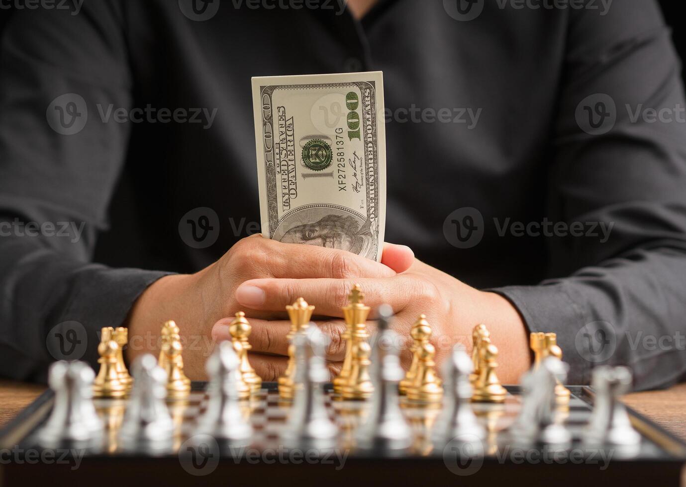 Businessman holding money in hand and looking at a chess game photo