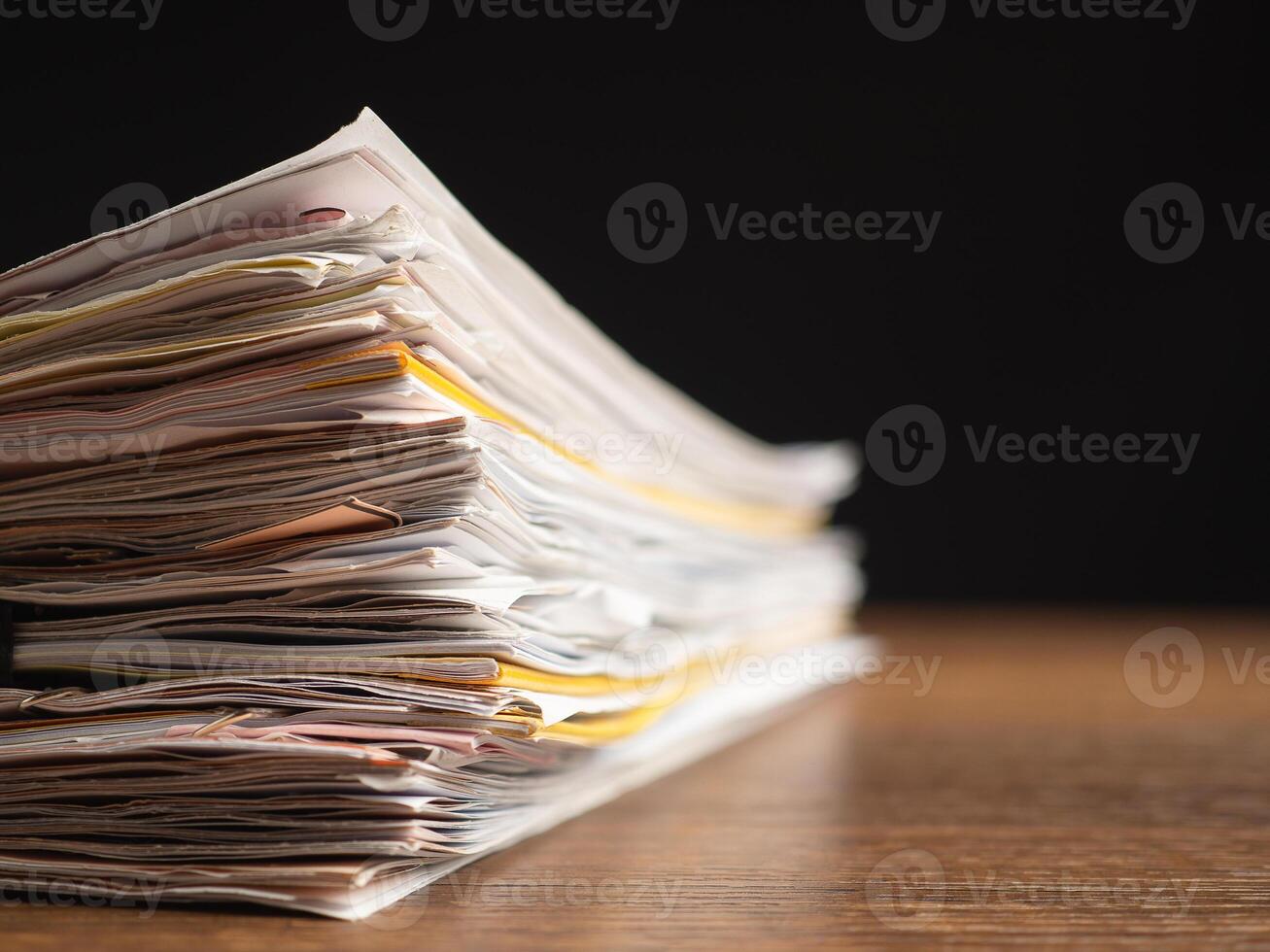 Stack of documents with binder clips on a wooden table with a black background photo
