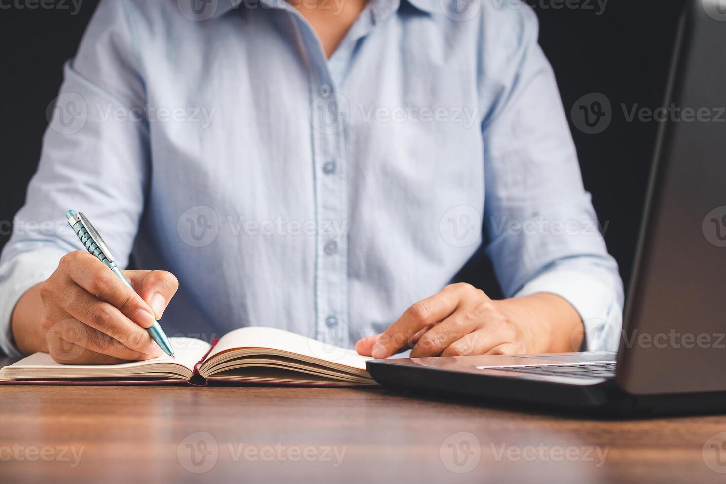 Close-up of a businessman holding a pen writing on paper on a desk while sitting in the office photo