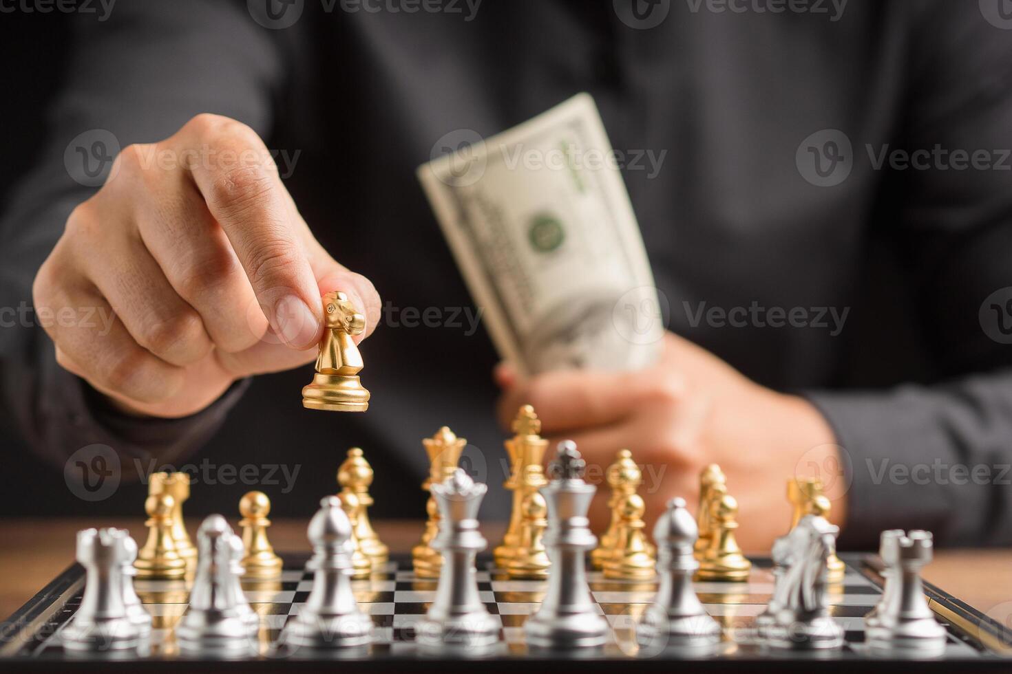 Businessman playing a game of chess and holding money in hand photo