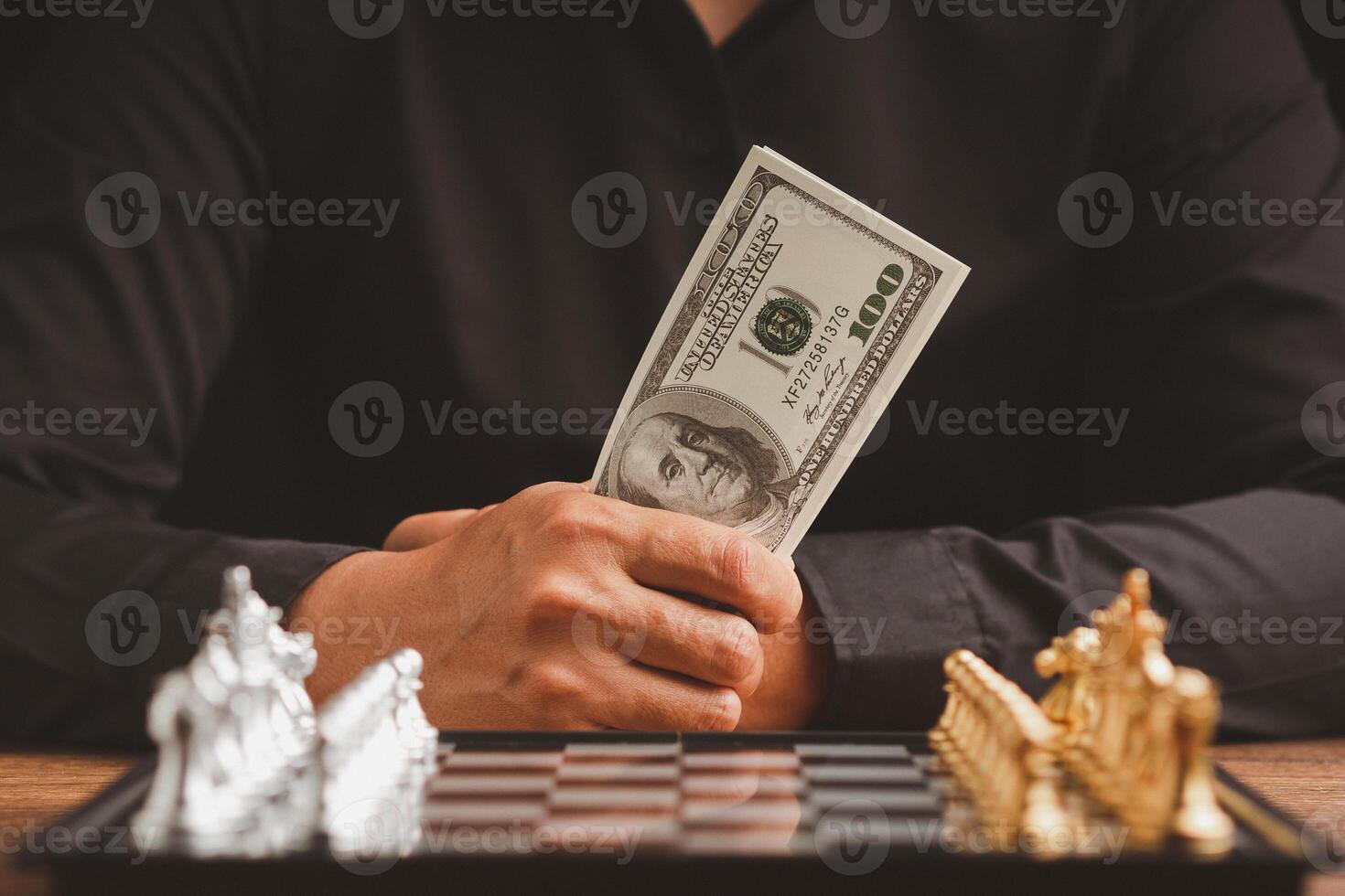Businessman holding money in hand and looking at a chess game photo