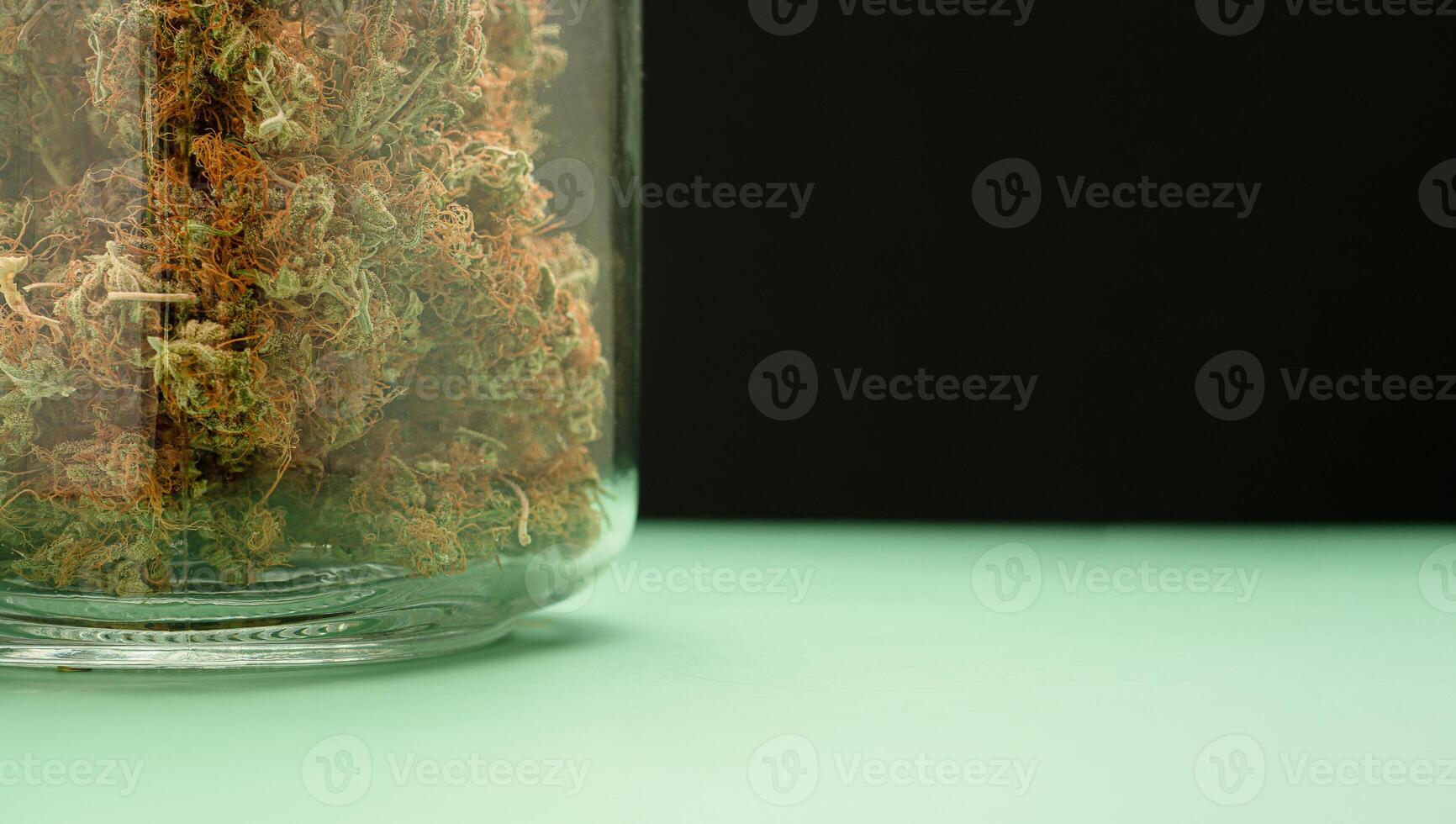 Dry cannabis buds flower in a jar glass on a green floor with a black background. photo