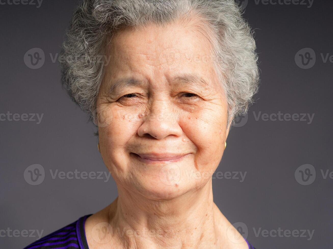 Cheerful an elderly Asian woman with short gray hair looking at the camera with a smile while standing on gray background in the studio. photo
