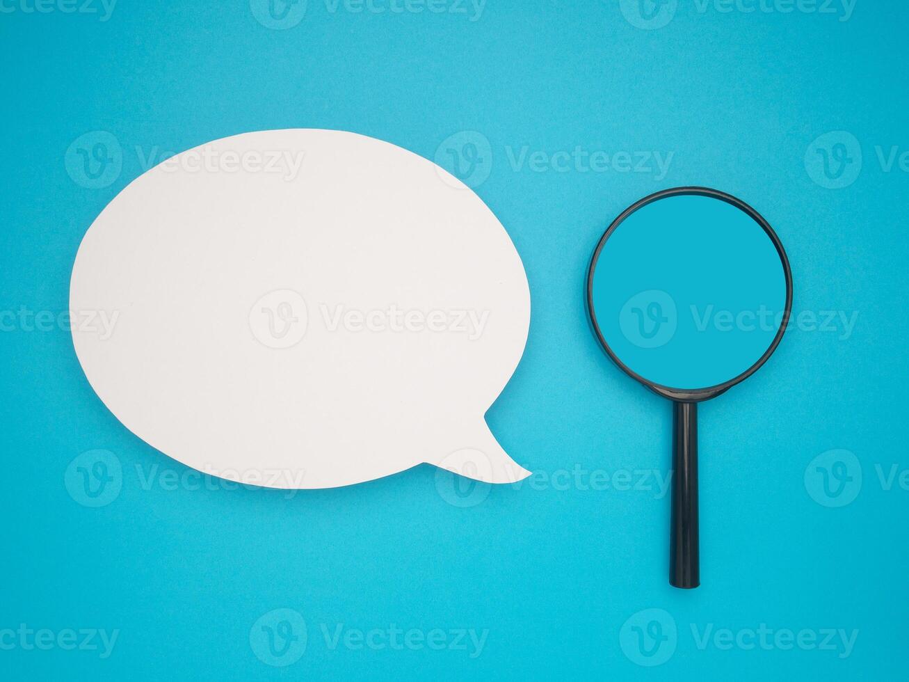 Top view of a blank speech bubble and a magnifying glass on a blue background photo