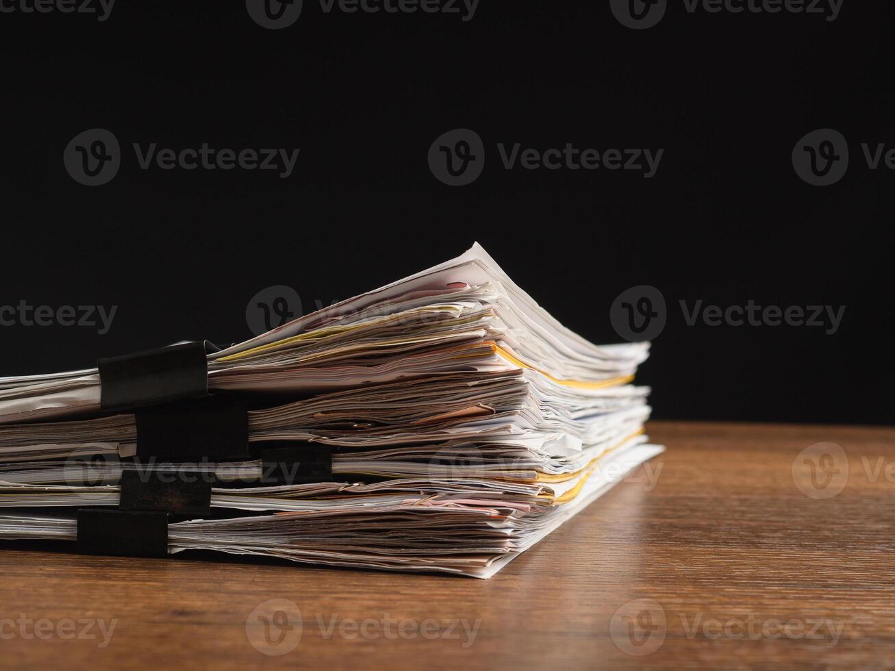 Stack of documents with binder clips on a wooden table with a black background photo