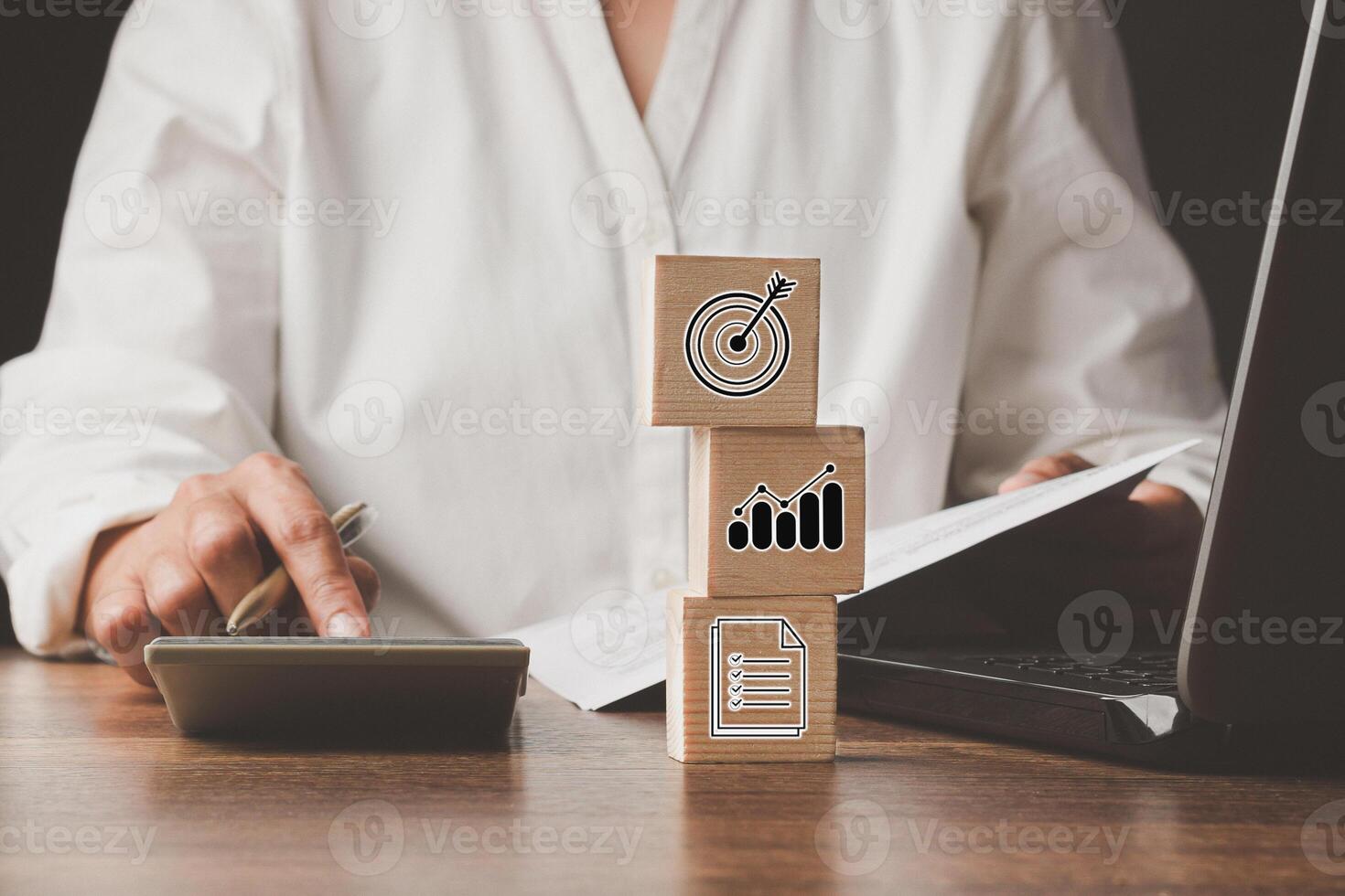 Woman using a calculator and three wooden cubes with icons business on the table in the office photo