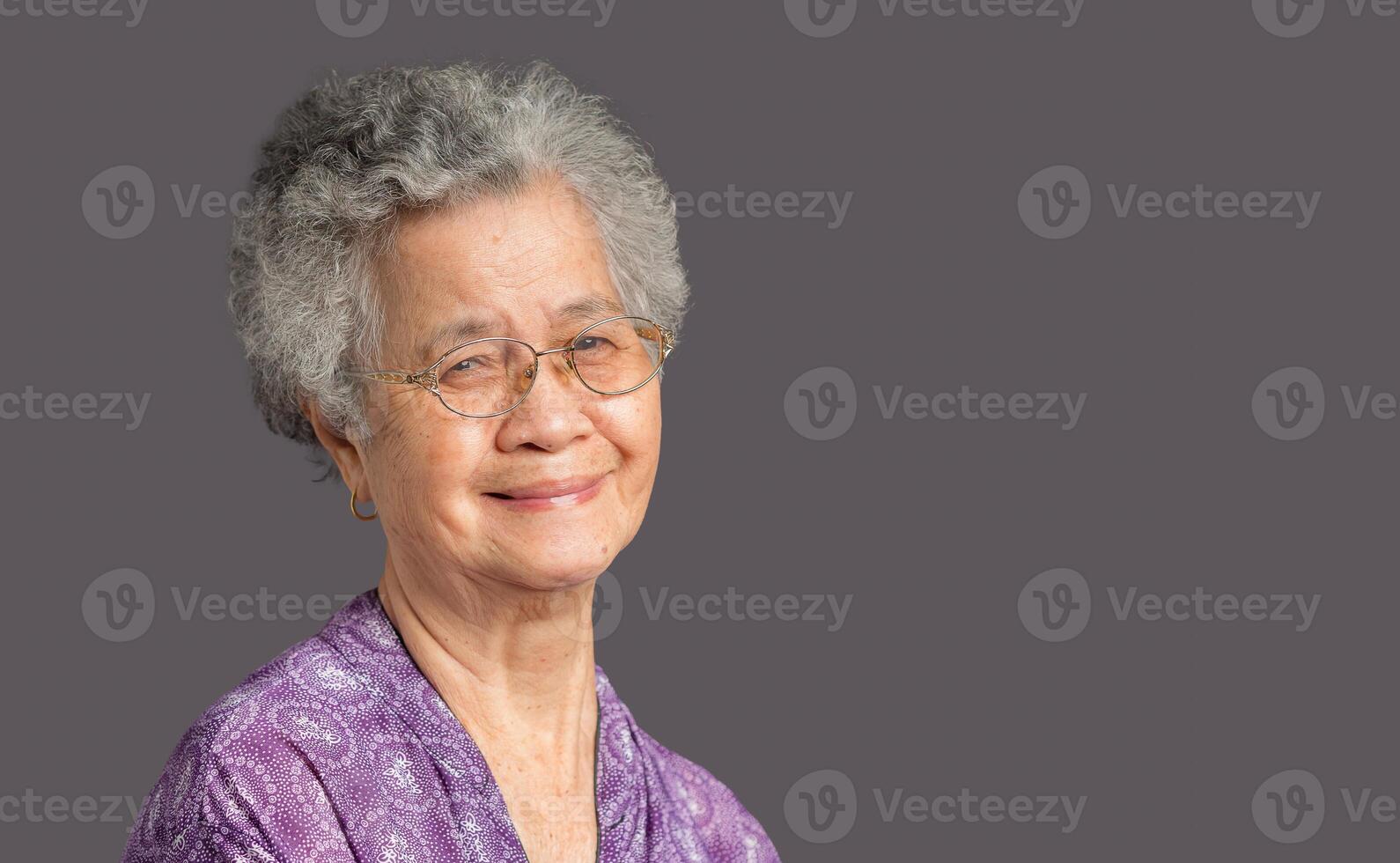 Cheerful an elderly Asian woman with short gray hair looking at the camera with a smile while standing on gray background in the studio. photo