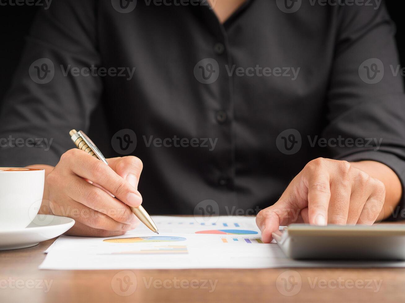 Close-up of a businessman holding a pen writing on paper on a desk while sitting in the office photo