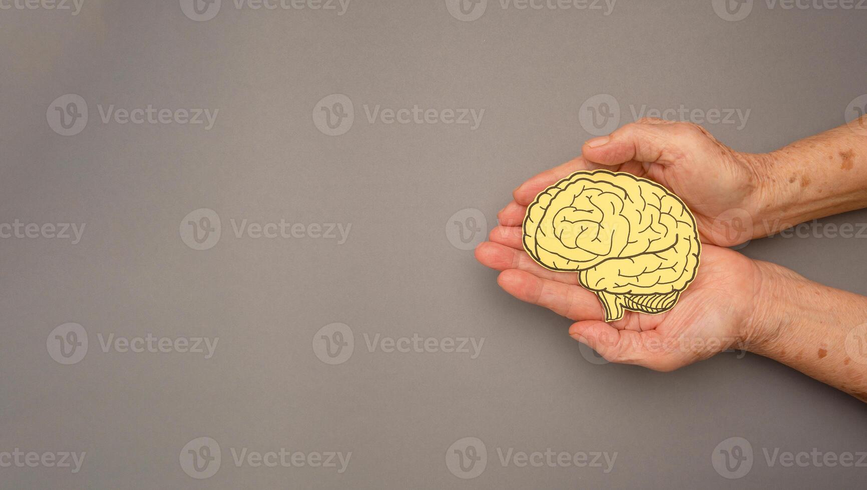Brain shape made from paper on a palm senior woman on a gray background photo