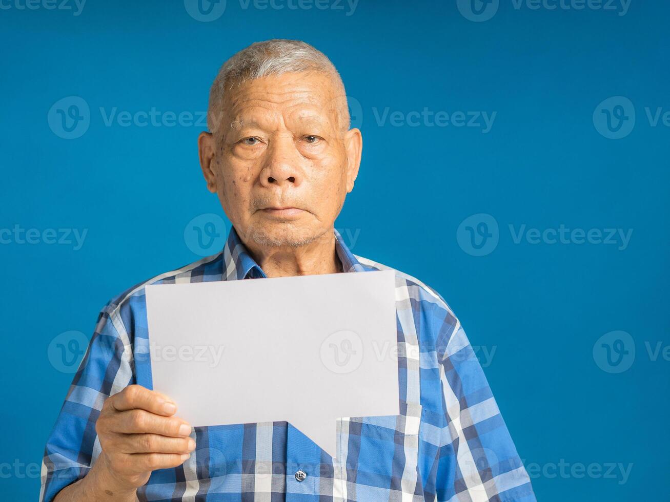 Senior man holding a blank speech bubble while standing on a blue background photo