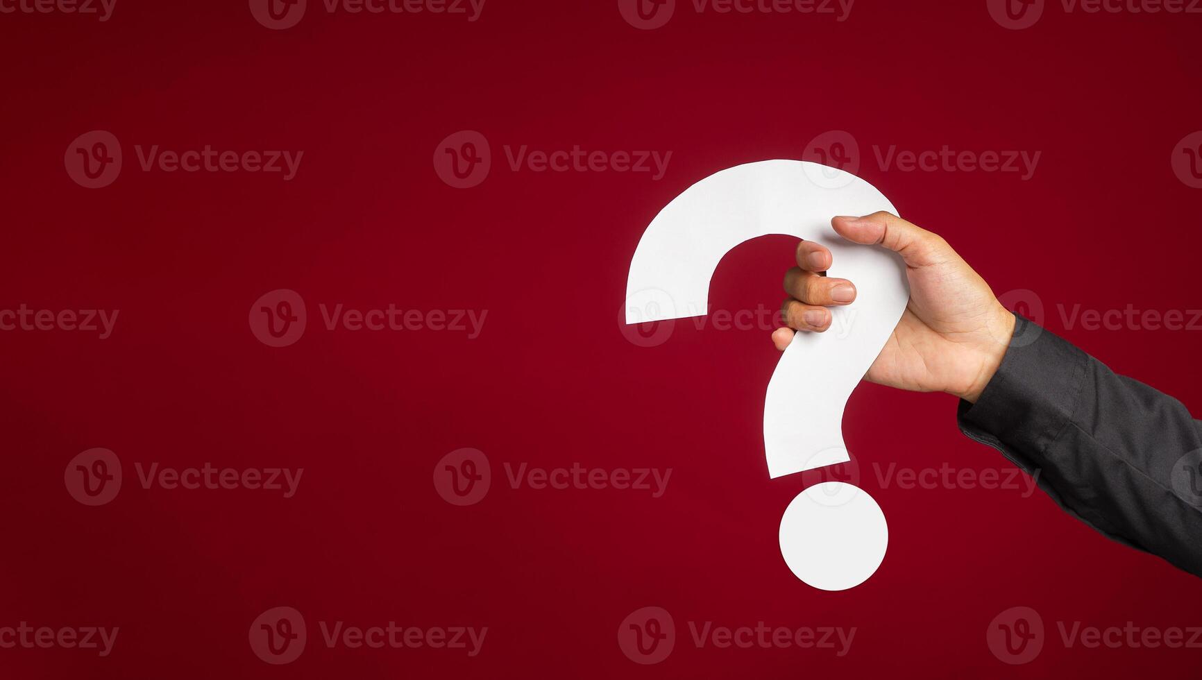 Hand of a man in a black shirt holding a white question mark while standing with a red background photo