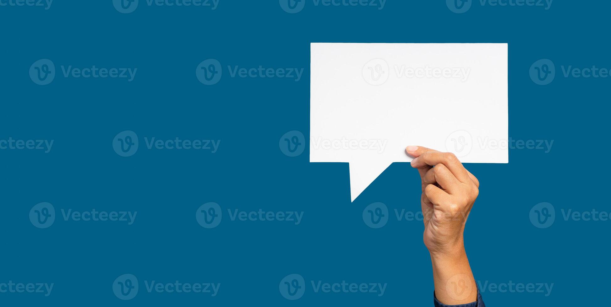 A speech bubble concept. Hand holding of an empty white speech bubble against a blue background. photo