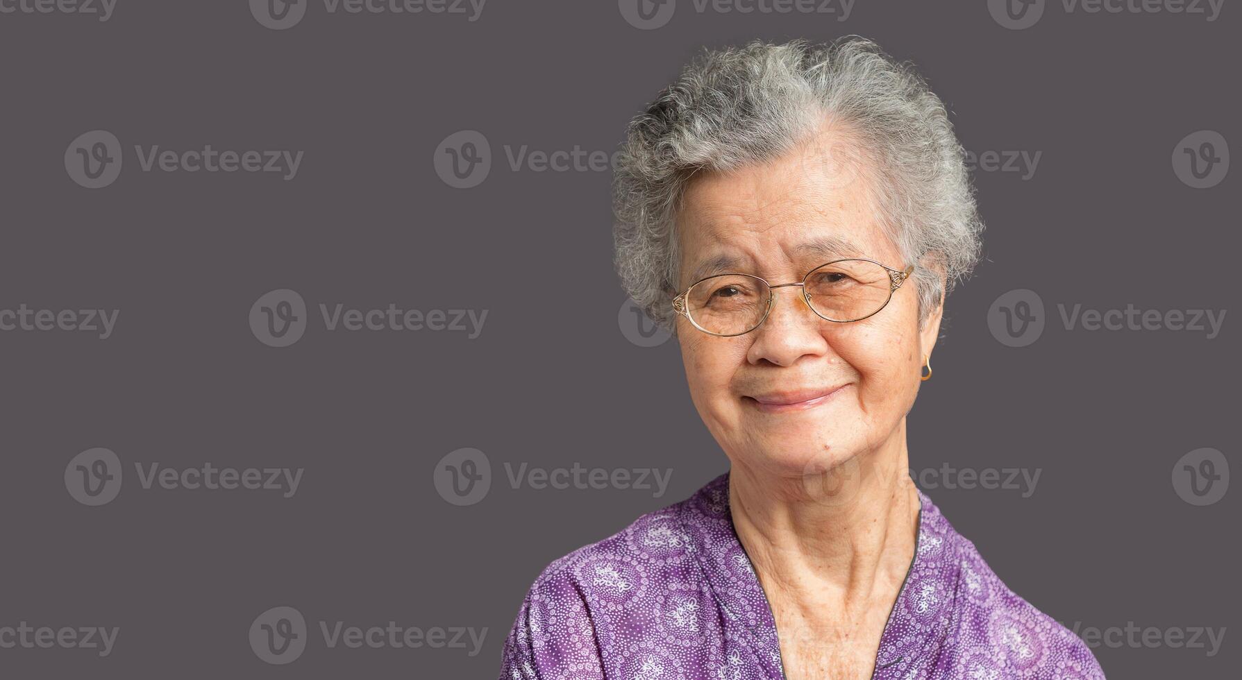 An elderly Asian woman looking at the camera with a smile while standing against on gray background photo