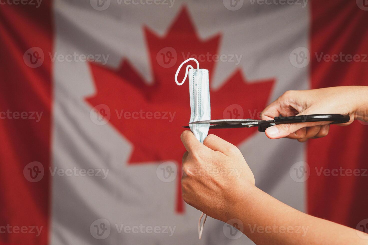 End of COVID-19 or Coronavirus. Close-up of a medical mask in a fist over on Canada flag background. End of quarantine back to Normal life photo