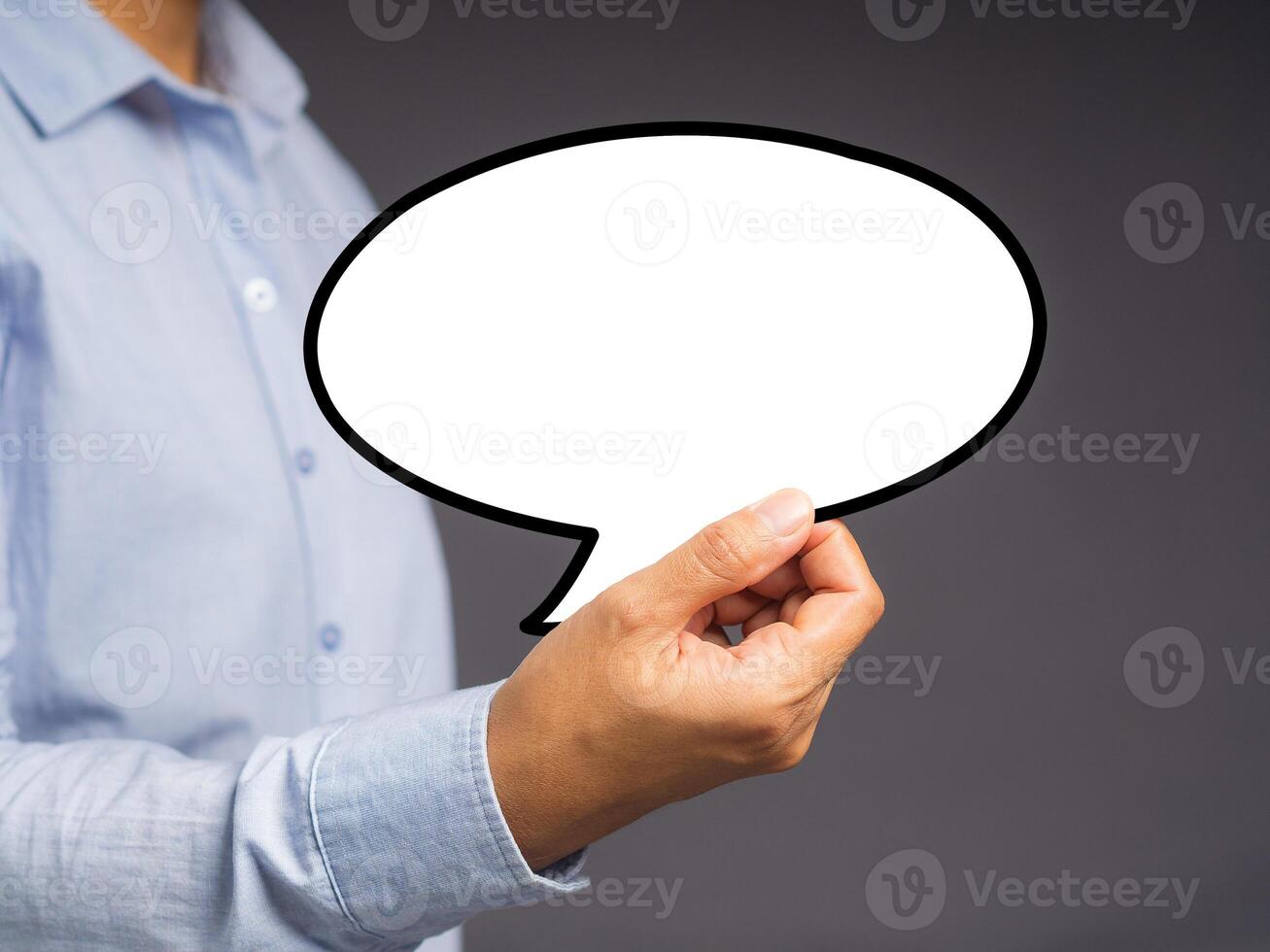 Hand holding of an empty white speech bubble against a gray background. photo