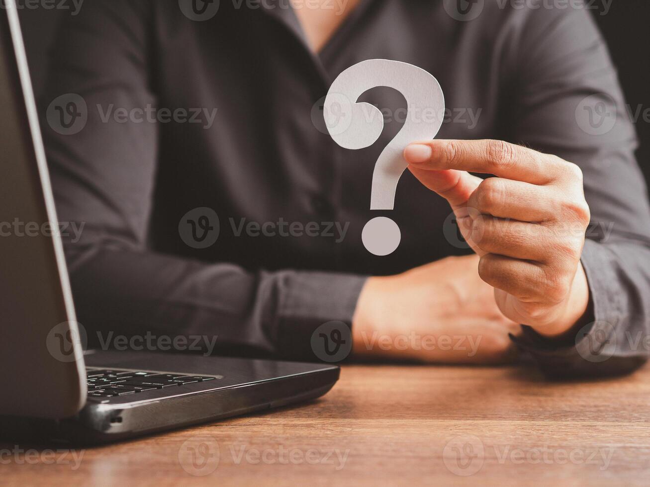 Focus on the hand of a businessman holding a white question mark paper while sitting in the office photo