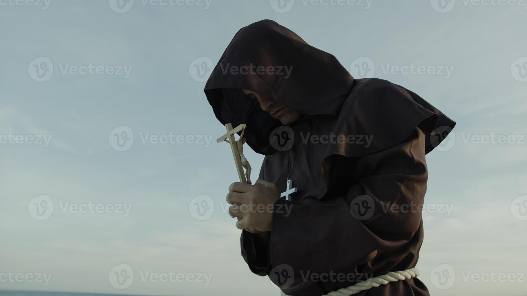 Religious Monk Prays With A Crucifix Of Jesus In His Hand Kneeling On The Sand photo