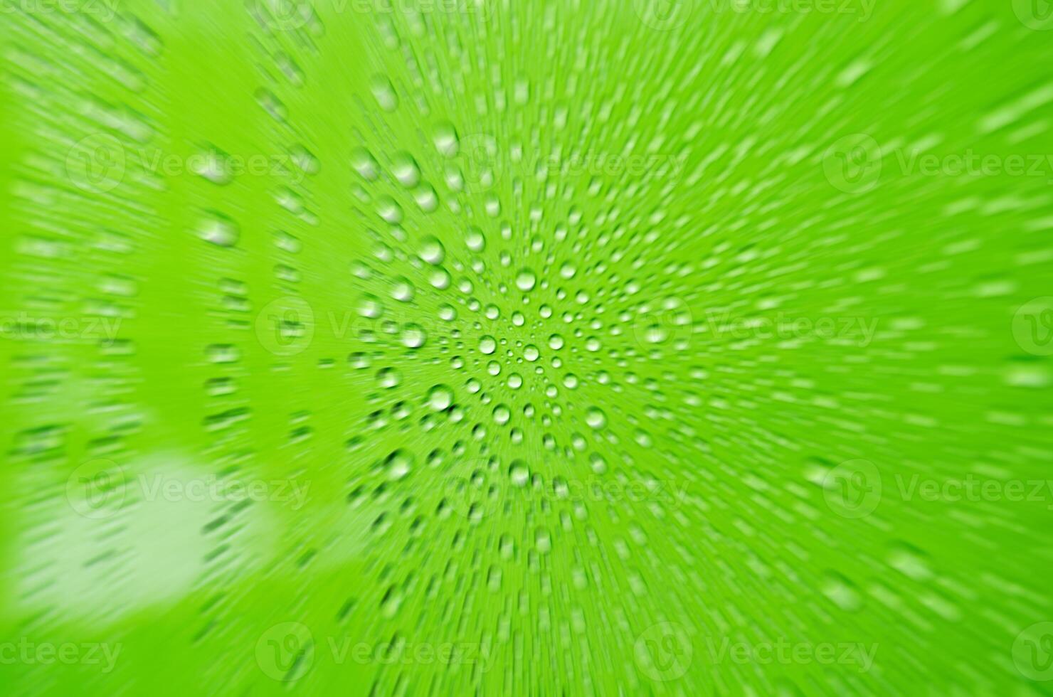 Zooming into rain water droplets on green glass background. Close up of rain drop from below photo