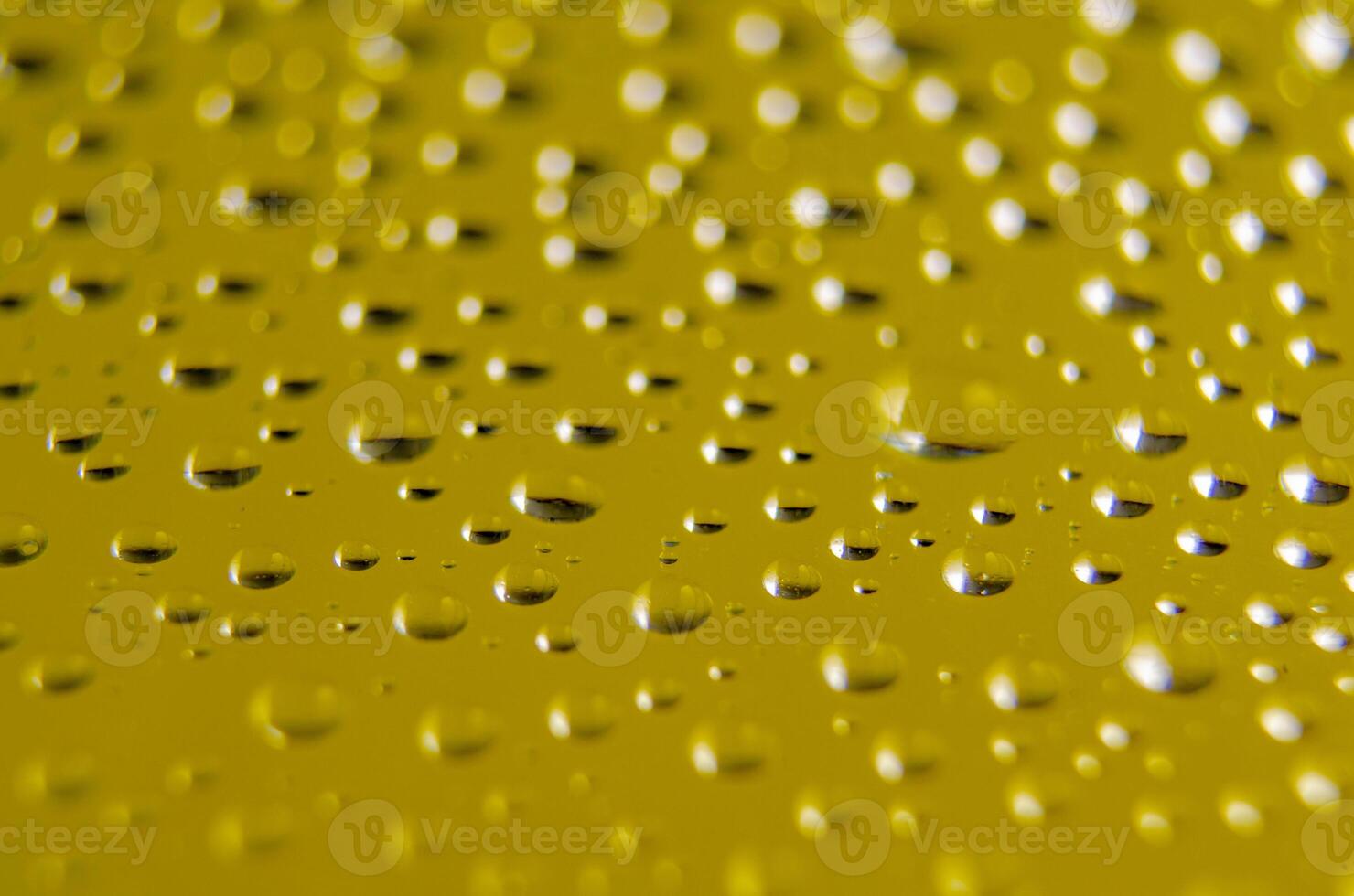 Side view of raindrops forming patterns on a smooth surface on yellow background. Fresh rain texture photo