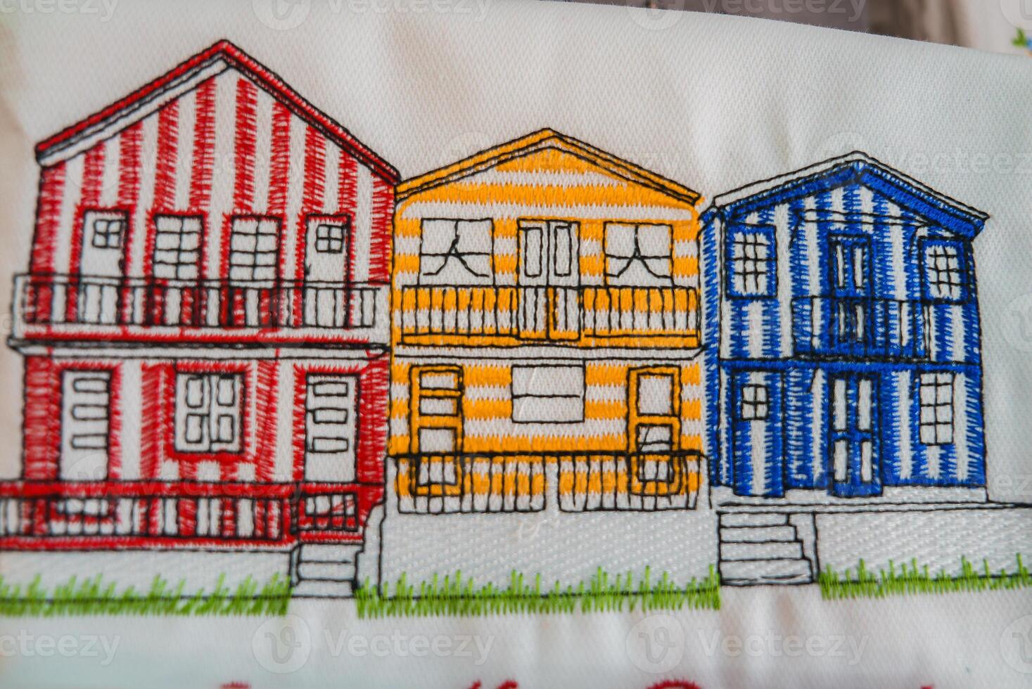 Detailed embroidery of three vibrant Costa Nova beach houses in Aveiro, Portugal. Features red, yellow, and blue vertical stripes, balconies, and multiple windows. photo