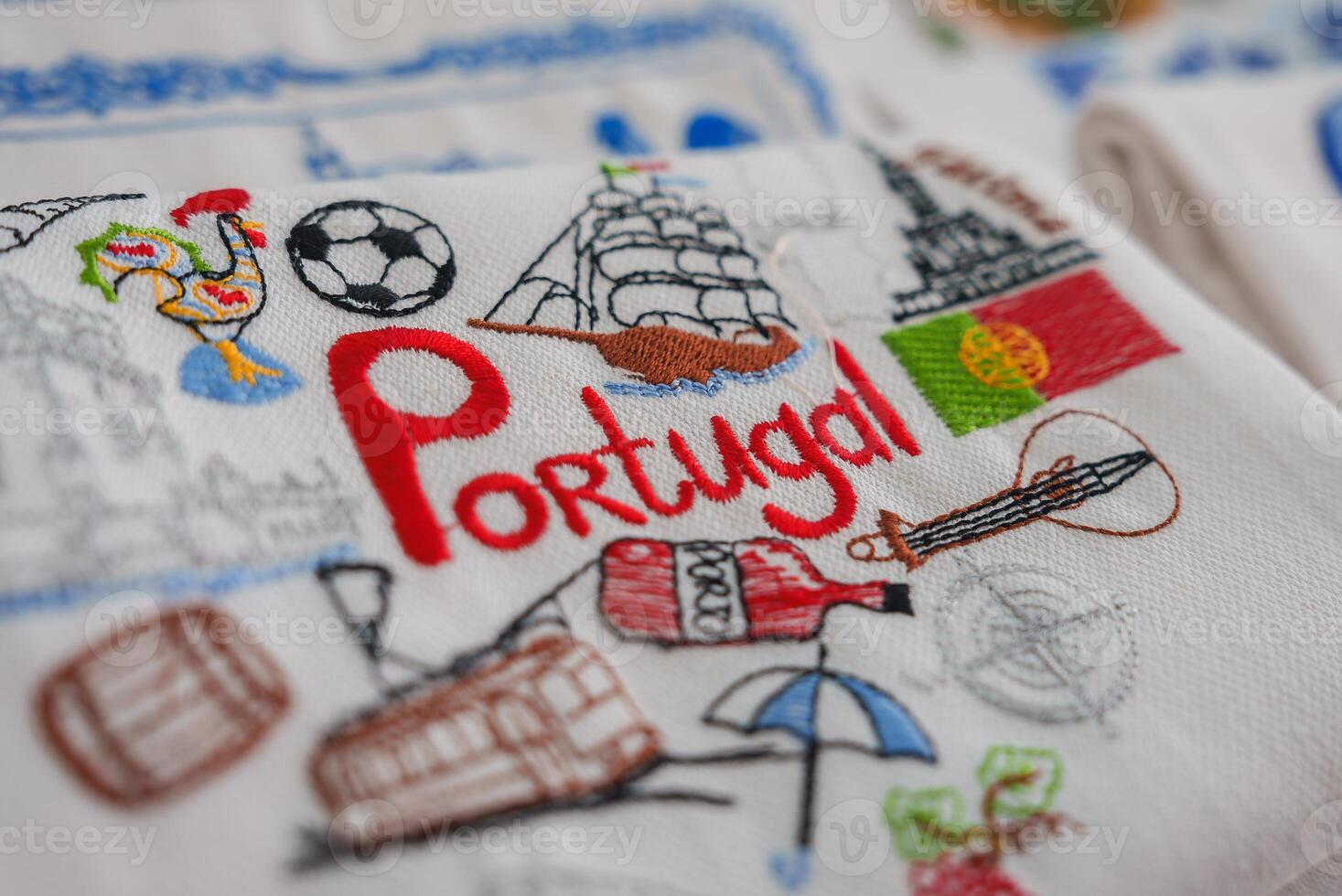 Intricately stitched fabric featuring the word Portugal, a rooster, a soccer ball, a tram, a ship, an umbrella, and the Portuguese flag, representing Portuguese heritage. photo