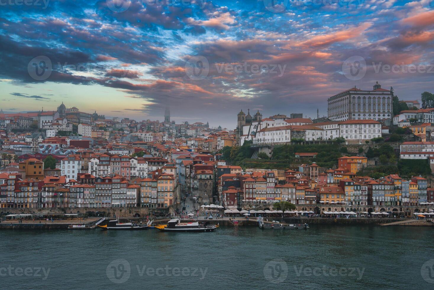 View of Porto, Portugal, featuring the colorful Ribeira district, Clerigos Tower, and Episcopal Palace. Traditional Rabelo boats dot the Douro River under dramatic clouds. photo