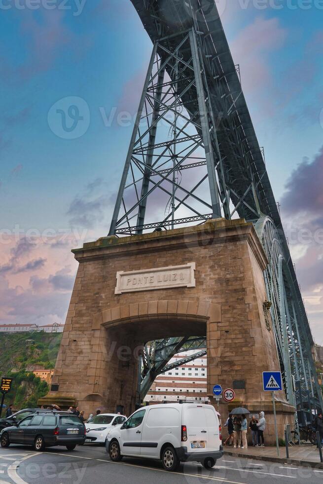 The iconic Ponte Luiz I bridge in Porto, Portugal, features a double-deck iron structure and a massive stone archway. Vehicles and pedestrians add to the bustling scene. photo