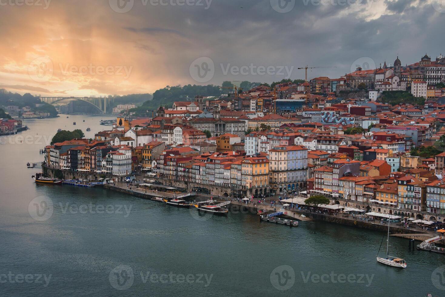 Colorful buildings with red-tiled roofs cascade down to the Douro River in Porto, Portugal. The Dom Luis I Bridge spans the river, connecting to Vila Nova de Gaia. photo