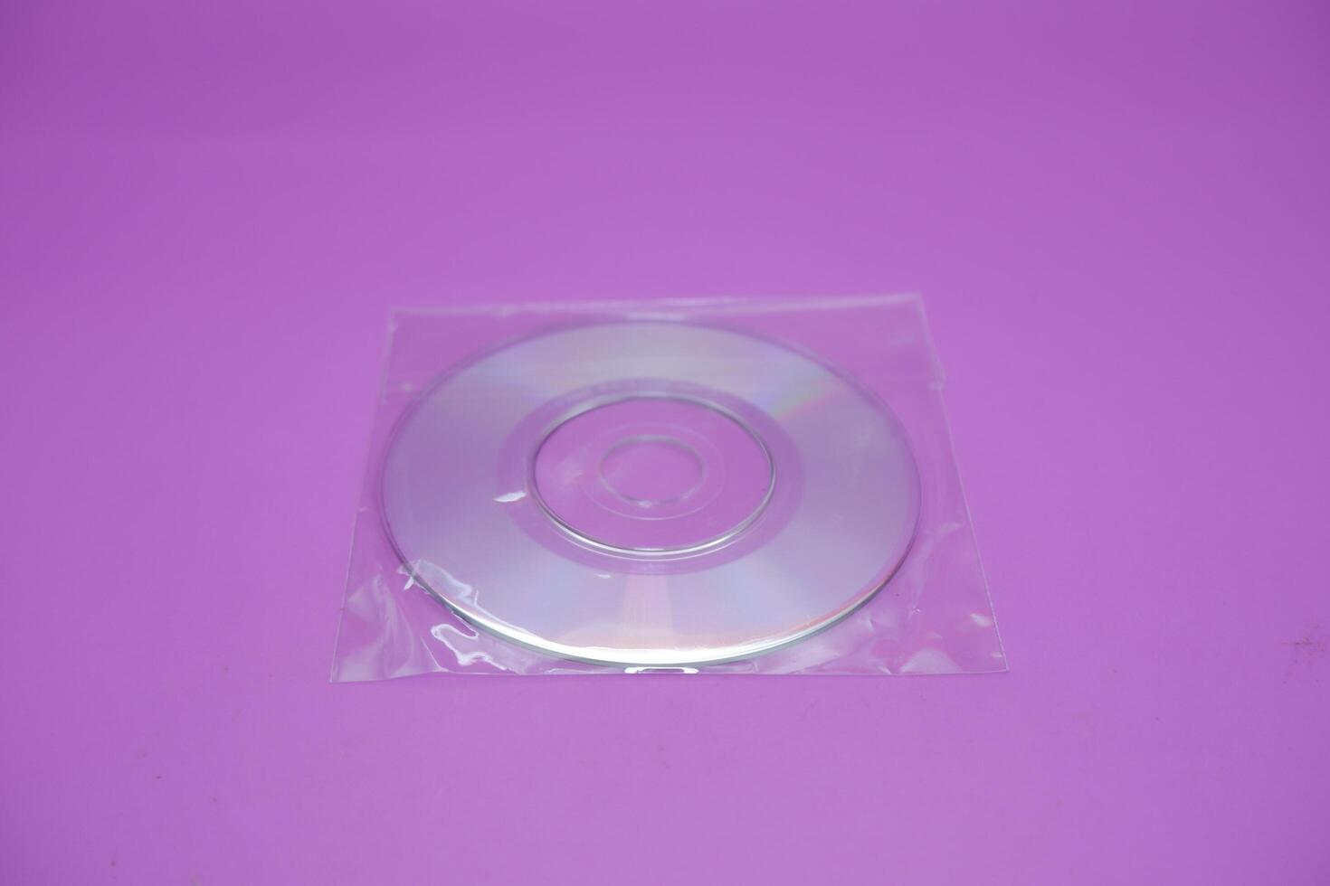 A compact disc isolated on a purple background. A compact disc wrapped in clear plastic. photo