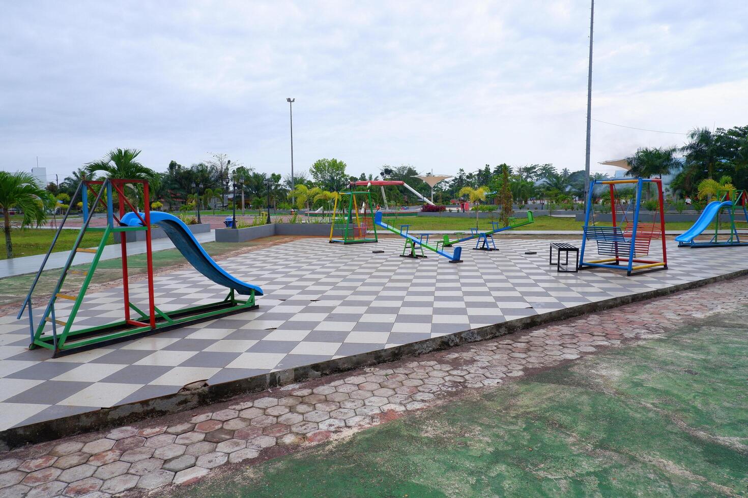 a playground in the park consisting of slides, seesaws, and hanging chairs. photo