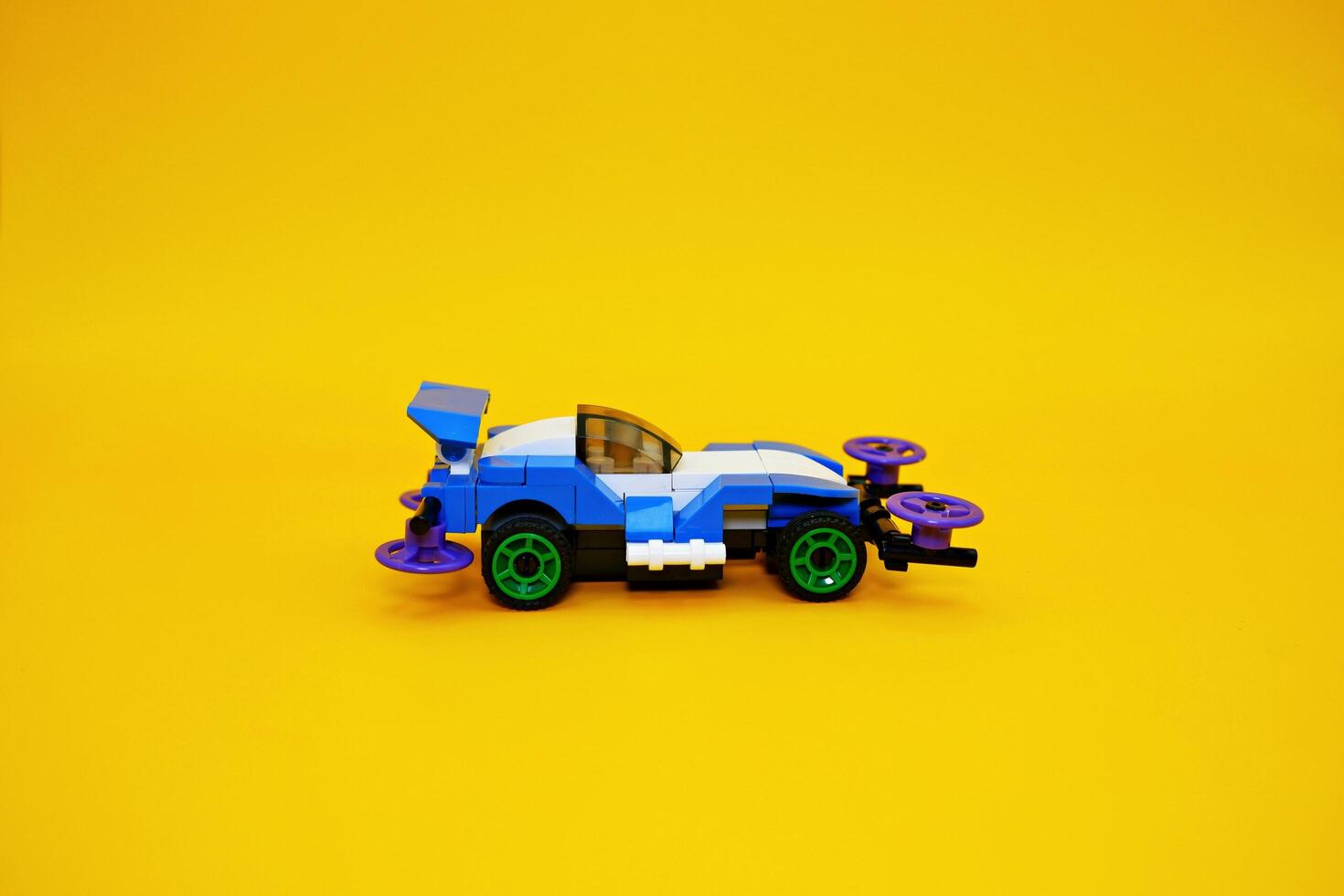 blue racing car assembled from plastic blocks. toy car isolated on yellow background photo
