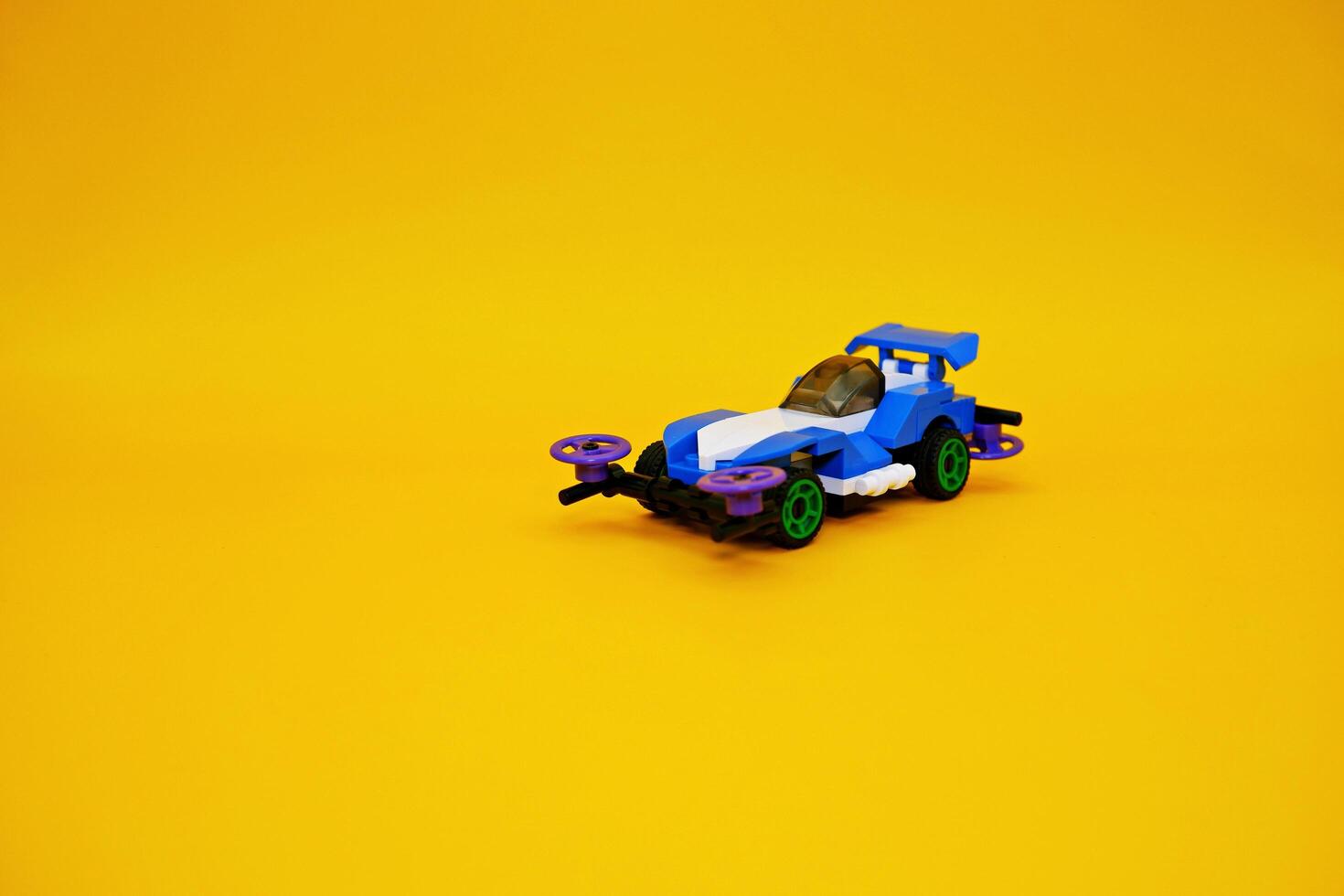 blue racing car assembled from plastic blocks. toy car isolated on yellow background photo