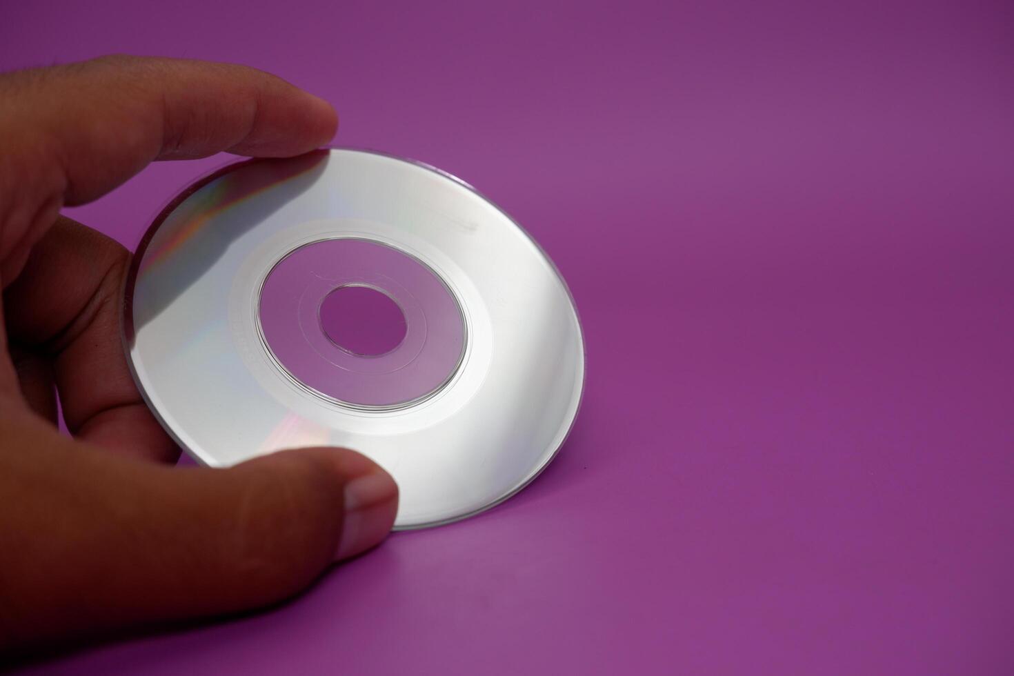a hand holding a compact disc. compact disc isolated on purple background. photo