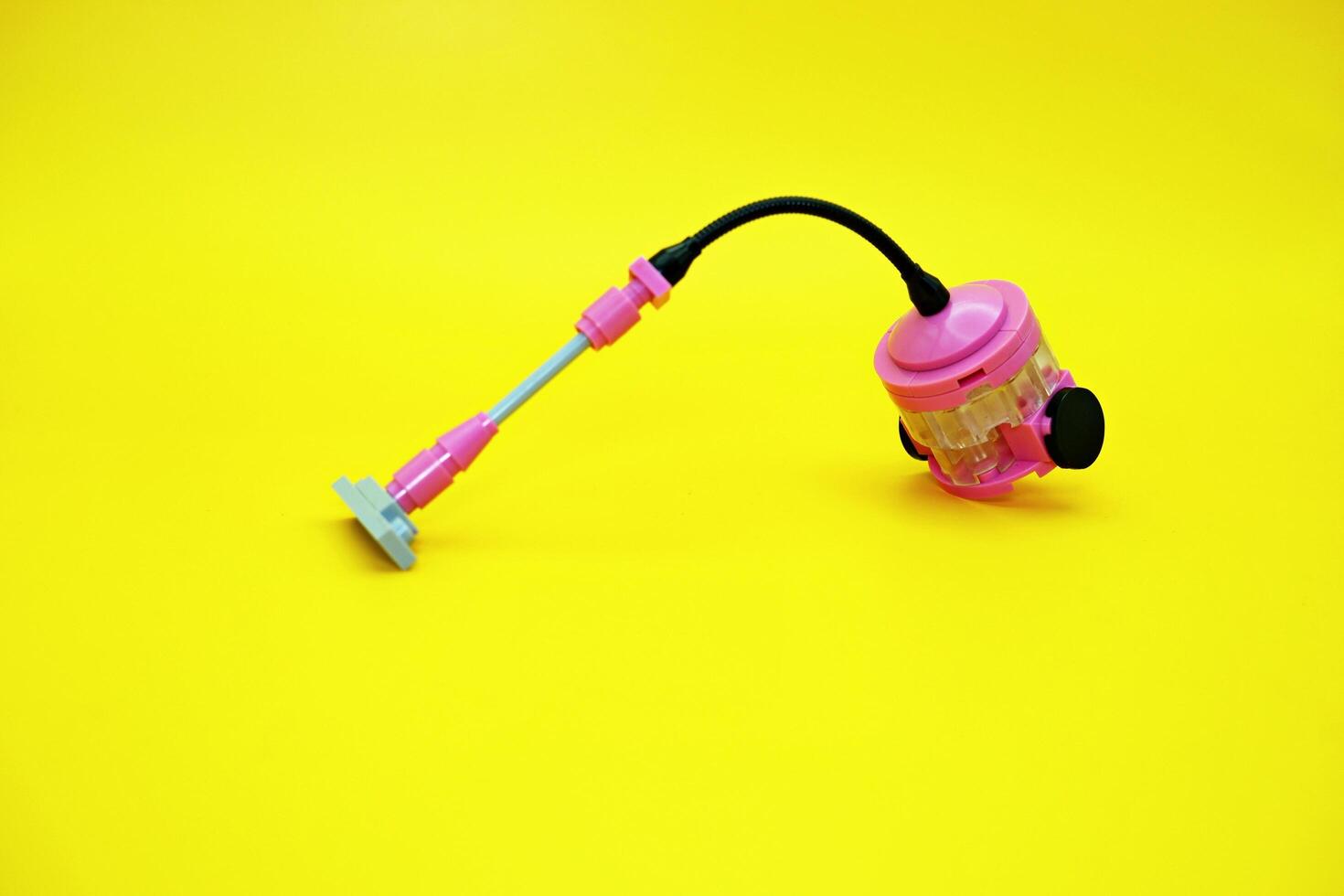 Mini vacuum cleaner toy assembled from plastic blocks. Vacuum cleaner toy isolated on yellow background. photo