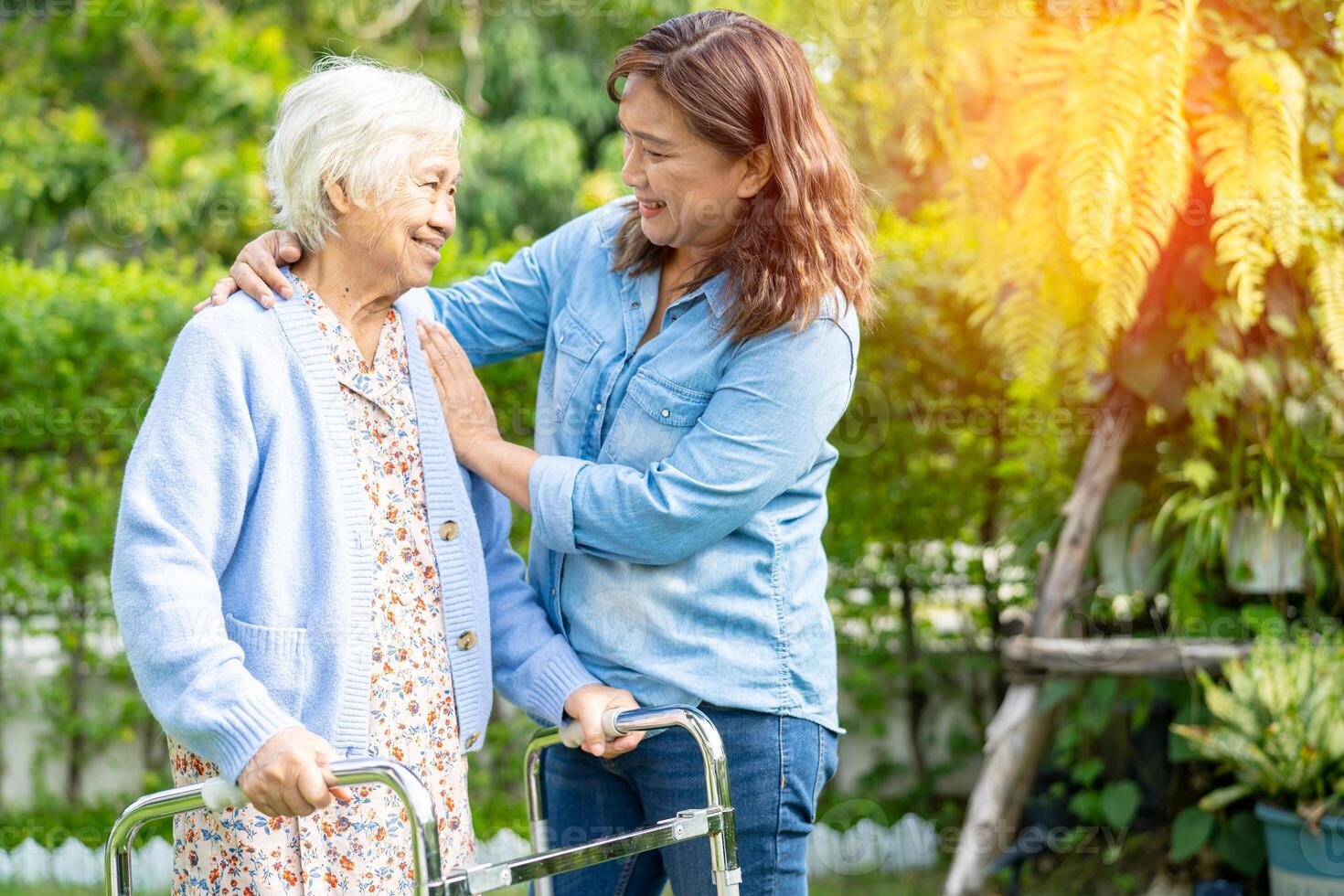 Doctor caregiver help and care Asian senior woman patient walk with walker in park at hospital. photo