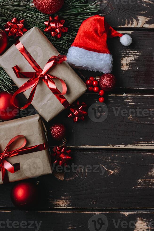 Top view photo Christmass flatlay gift boxes,red christmas tree toys,Santa hat and spruce brance on wooden background. Xmas backdrop with space for text.Copyspace.Vertical photo.