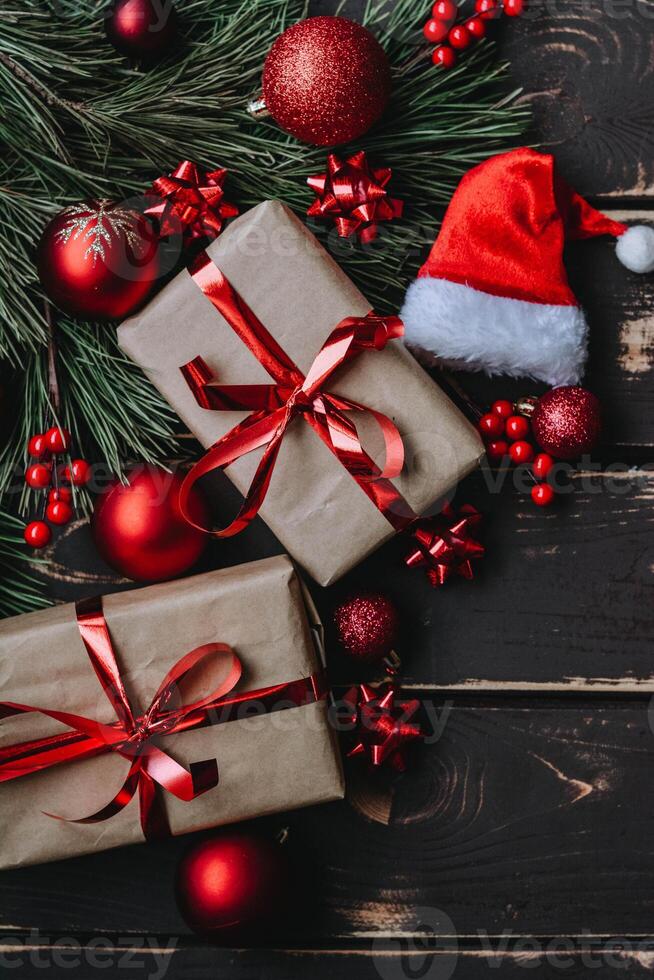 Top view photo Christmass flatlay gift boxes,red christmas tree toys,Santa hat and spruce brance on wooden background. Xmas backdrop with space for text.Copyspace.Close up.Vertical photo.