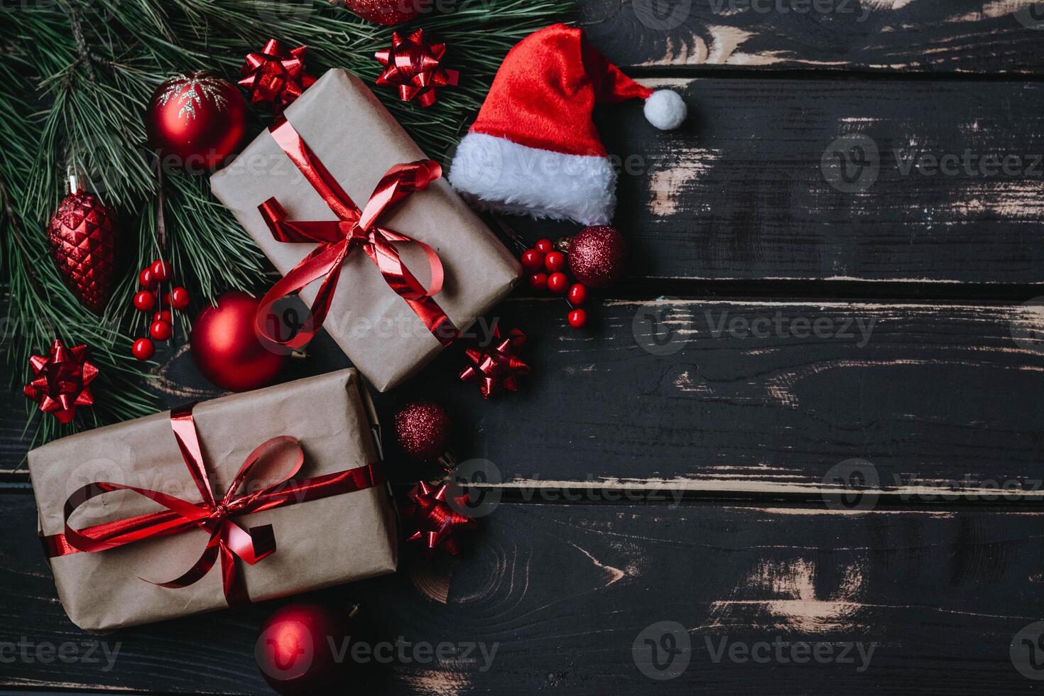 Top view photo Christmass flatlay gift boxes,red christmas tree toys,Santa hat and spruce brance on wooden background. Xmas backdrop with space for text.Copyspace.