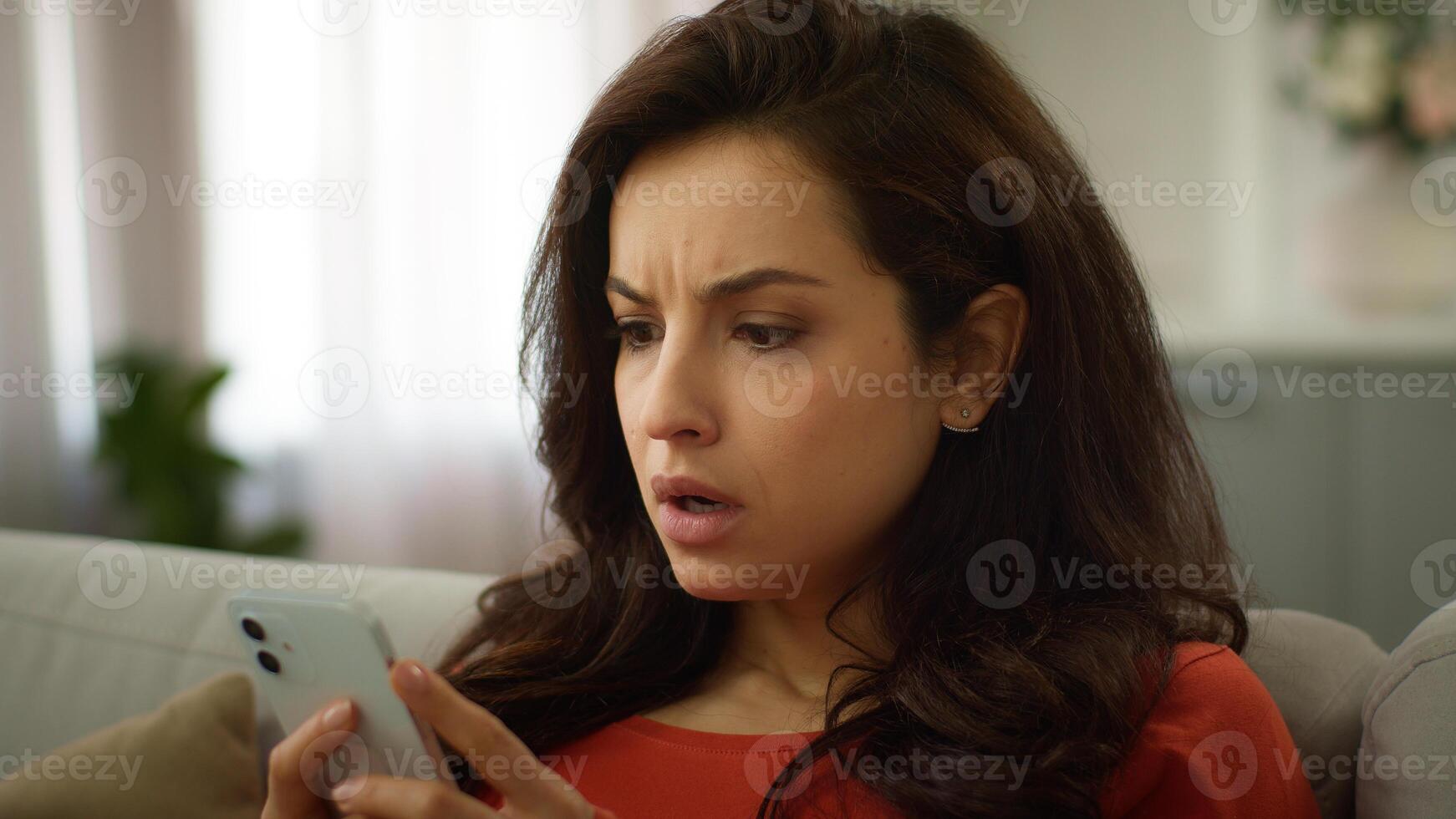Shocked mad displeased Caucasian woman stressed nervous female girl use mobile phone chatting app texting online receiving bad message SMS smartphone error connection problem losing game at home sofa photo