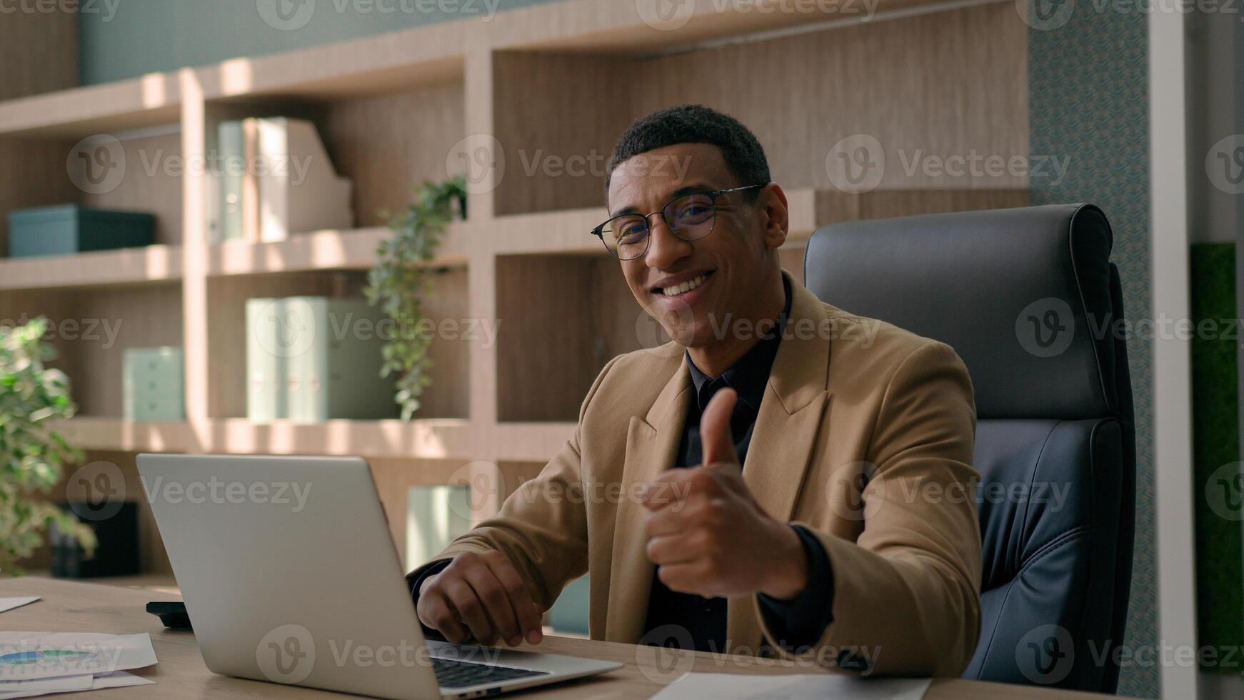 African American 30s millennial business man happy businessman smiling entrepreneur office manager working laptop typing on computer looking camera smile show thumb up gesture aprove recommend like photo